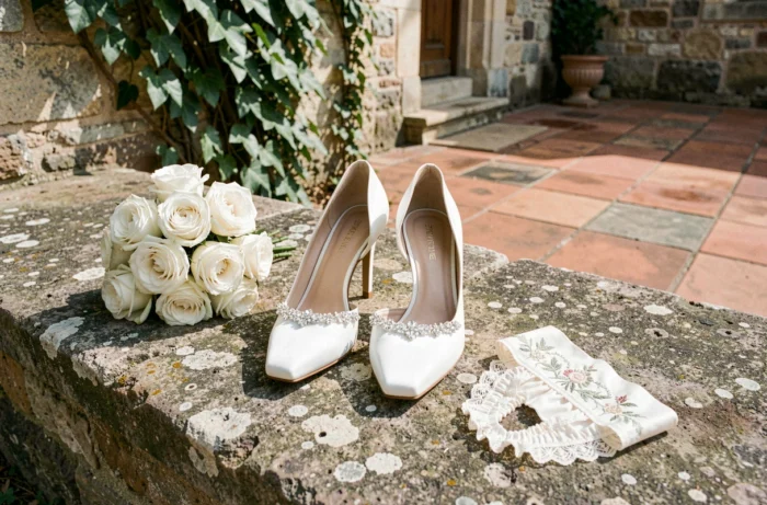 Escarpins de mariée en satin blanc ornés de cristaux et jarretière brodée sur les marches d'un château français
